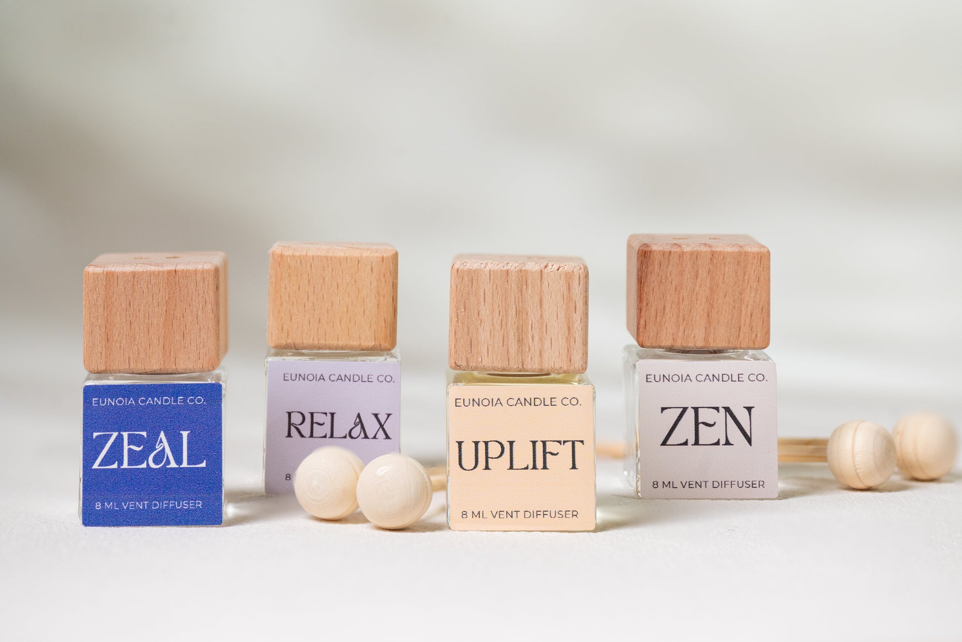 Four small vent diffusers with wooden caps labeled 'ZEAL', 'RELAX', 'UPLIFT', and 'ZEN' on a light background.