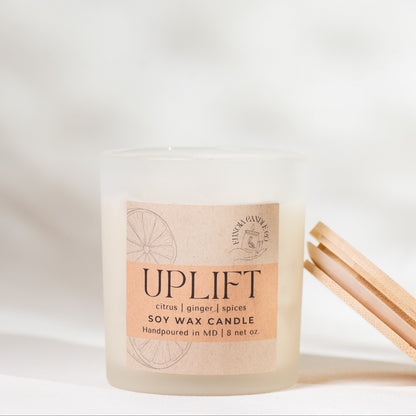 Candle labeled 'Uplift' with wooden matches on a soft white background