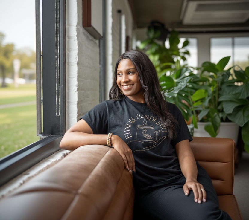Woman sitting on a couch wearing a black t-shirt with a graphic design, surrounded by plants.