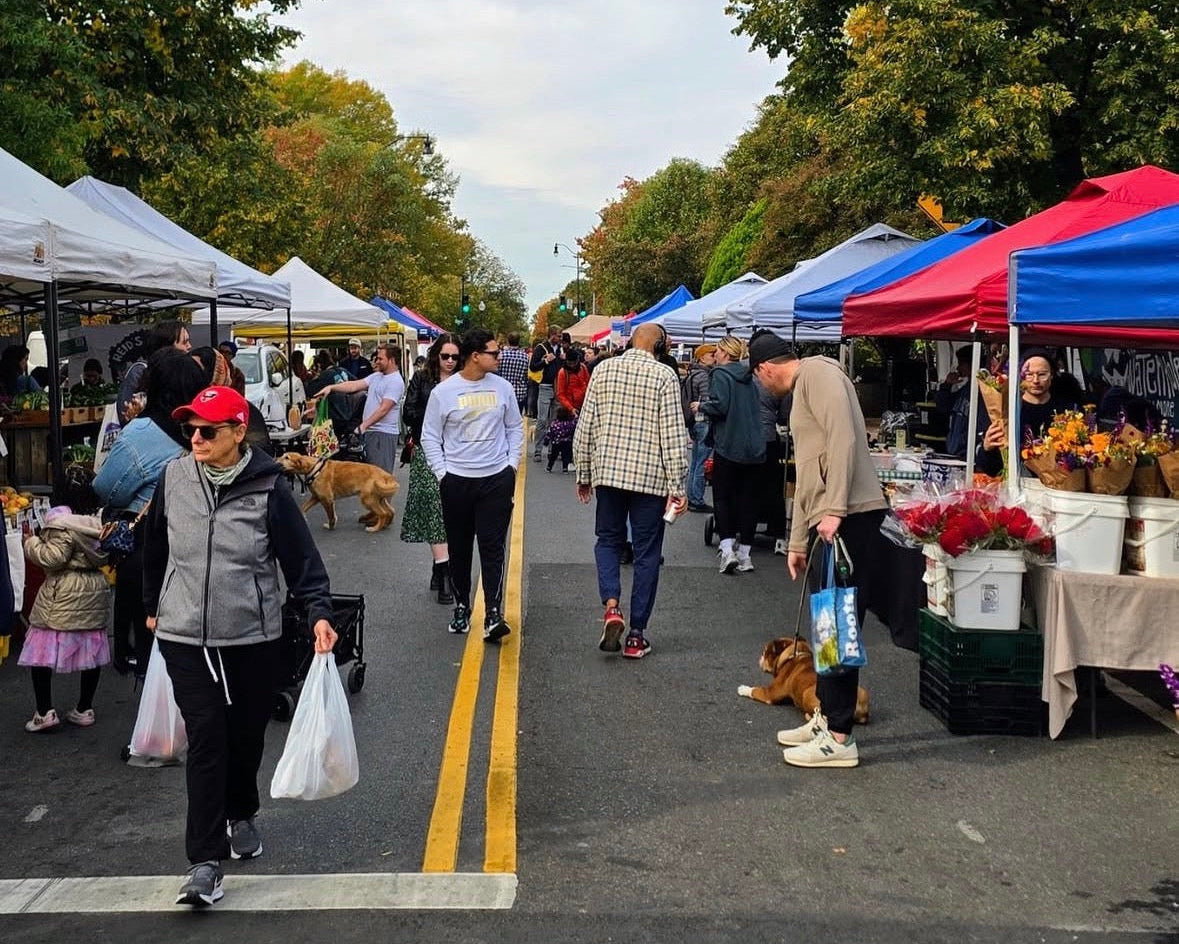 Outdoor market with people shopping under colorful tents on a sunny day.